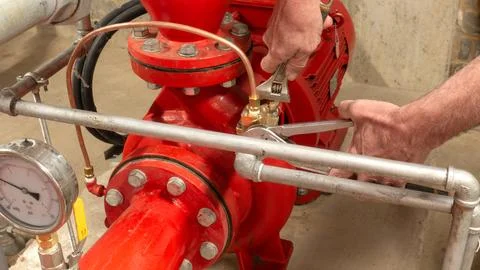 Sprinkler engineer replacing a valve on a red pump set using spanners. Stock Photos