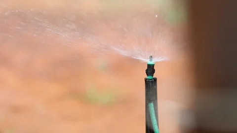Sprinkler head spraying water slowly defocuses behind object, close-up Stockbeeldmateriaal 333631253