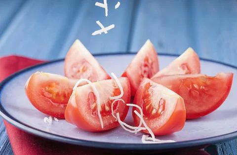 Sprinkling cheese on tomatoes. Stock Photos
