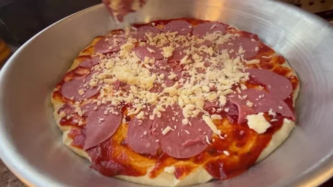 Sprinkling Shredded Cheese Over Sliced Meat and Sauce on Pizza Dough Tray Stock Footage 344786460