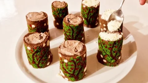 Sprinkling white sugar powder on mini christmas tree cake rolls for snow effect Stock Footage 327259187