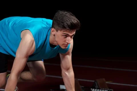 Sprinter leaving starting blocks on the running track in front of big modern Stock-Fotos
