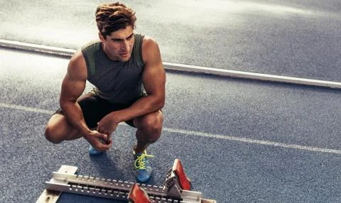 Sprinter sitting beside a starting block on running track Stock Photos