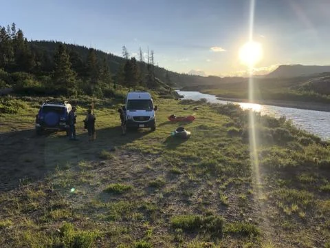 Sprinter Van and Off Road SUV Parked on Grass Alongside a River Stock Photos
