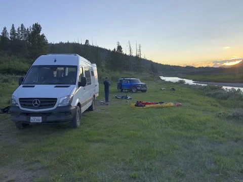Sprinter Van and Off Road SUV Parked on Grass Alongside a River Stock Photos