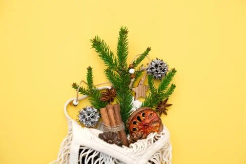 Spruce branch in an eco-friendly string bag and Christmas decorations on yellow Stock Photos