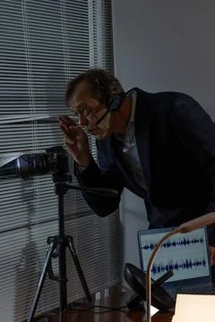 A spy with a headset and a camera peeks through the window for covert surve.. 写真素材