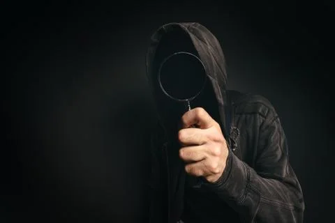 Spyware computer software, hooded spooky person with magnifying glass Stock Photos