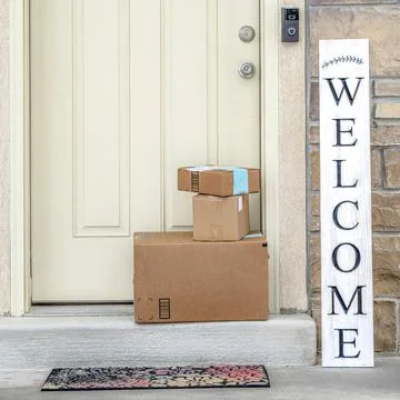 Square Boxes stacked in front of white wooden front door of home with welcome Stock Photos