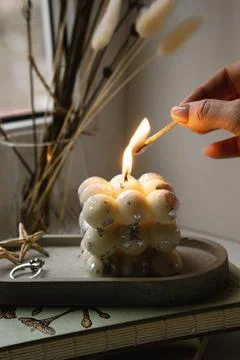 A square bubble candle is burning on a concrete stand. Woman lights the candle. Stock Photos