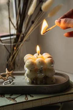 A square bubble candle is burning on a concrete stand. Woman lights the candle. Stock Photos