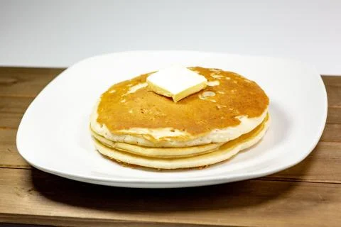 A square of butter laying onto of a stack of golden pancakes Stock Photos