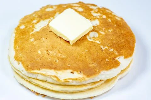 A square of butter laying onto of a stack of golden pancakes Stock Photos