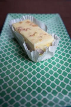 Square cake slice with icing and nuts on green plate, brown background Stock Photos