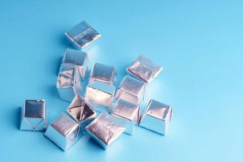 Square candies in a silver wrapper lying on a blue background Stock Photos