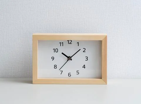 A square clock in front of a white wall Stock Photos