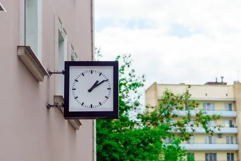 A square clock with hands on the building shows ten minutes past two Stock Photos