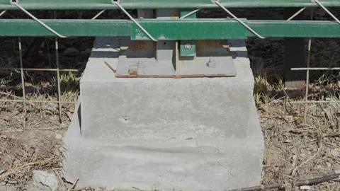 Square concrete base supporting a green metal fence post outdoors Stock Footage 332433514