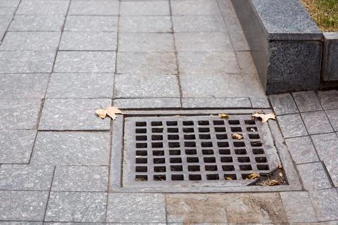 Square drainage storm grate system of city infrastructure pedestrian walkway. Stock Photos
