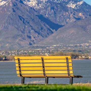 Square Empty bench overlooking a calm lake and snow capped mountain on a sunny Foto stock