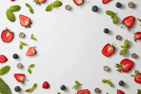 A square frame made of mint leaves, strawberries and blueberries on a gray Фото