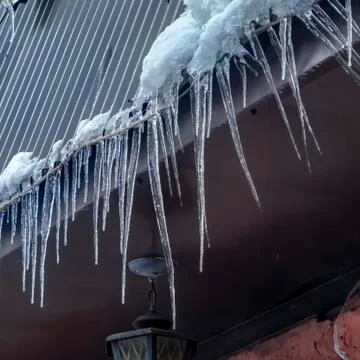 Square frame Spiked icicles at the edge of pitched gray roof with clumps of snow Stock Photos