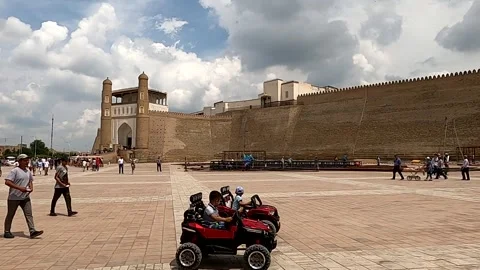 Square in front of the ancient Ark of Bukhara fortress with people and toy cars Stock Footage 336064264