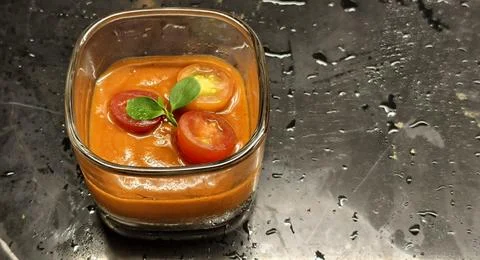 A square glass container filled with smooth orange tomato gazpacho 库存照片