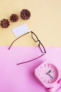Square glasses, alarm clock, pine tree flowers on a pastel pink and pastel ye Stock Photos