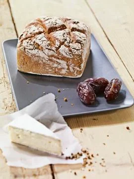 A square loaf of rye bread and dates on a ceramic platter with a slice of cheese Stock Photos