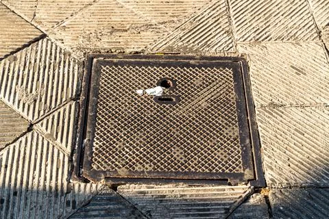 Square manhole cover with diamond pattern grid set into paved sidewalk in Bari, Stock Photos