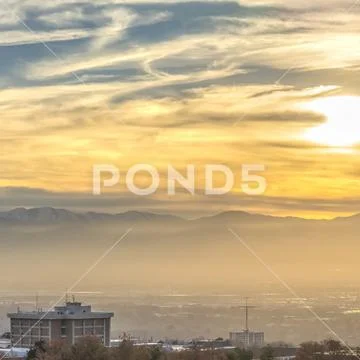 Square Panorama of a bustling city against a towering snowy mountain at sunset Stock Photos