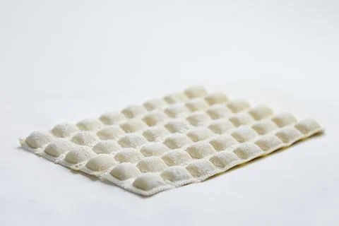 A square patch of freshly made uncooked ravioli covered in flour on a vibrant Stock Photos
