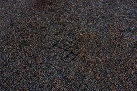 Square patterned footprint pressed into brown gravel on the ground. Stock Photos