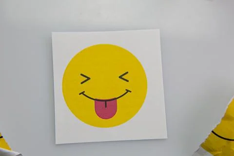 Square piece of paper with the face of a mocking emoji with tongue out. Stock Photos