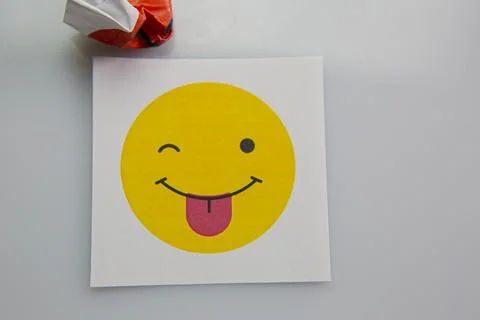 Square piece of paper with the face of a mocking emoji with tongue out. Stock Photos