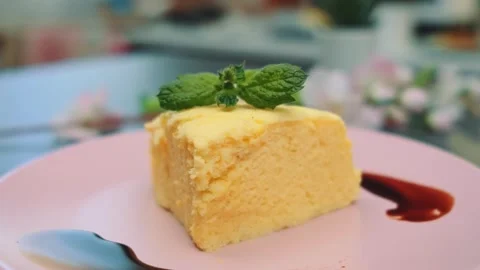 Square piece of yellow cake garnished with mint on pink plate indoors Stock Footage 342887390