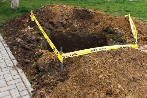 A square pit dug into the soil, next to public sidewalk and fenced with a r.. Stock Photos