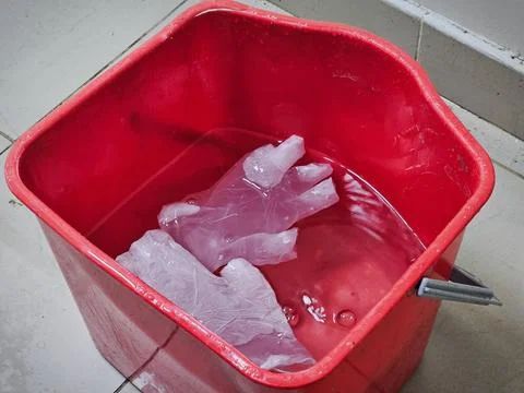 A square, red plastic bucket filled with water, containing two clear, discard Stock Photos