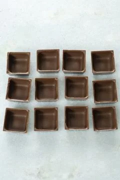 Square-shaped milk chocolate shells ready to be filled side view vertical. Stock Photos