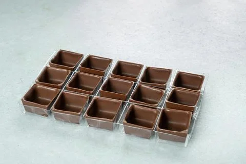Square-shaped milk chocolate shells inside the molds. Stock Photos