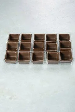 Square-shaped milk chocolate shells inside the molds top view vertical. Stock Photos