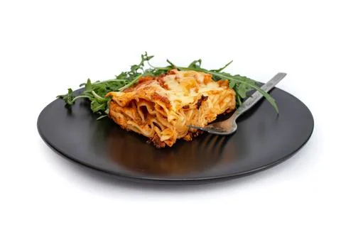 Square slice of lasagna on a black ceramic plate with arugula salad, soft f.. Stock Photos