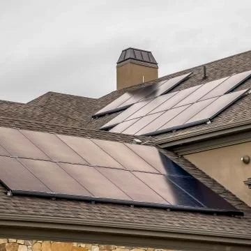 Square Solar panels mounted on the dark pitched roof of a home under cloudy gray Stock Photos