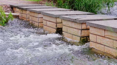 Square stone pier spans rushing garden stream landscape Stock Footage 340796057