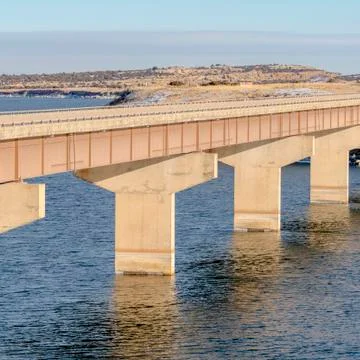 Square Stringer bridge spanning over calm lake with view of snowy land and Stock Photos