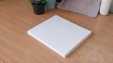 Square white canvas, book without inscriptions lying on wooden table on interior Stock Photos