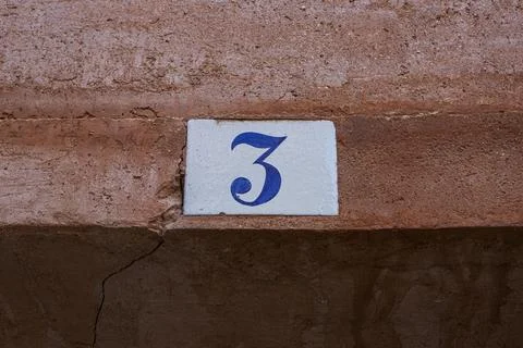 Square white ceramic brick on old wall with the number three painted in blu.. Stock Photos