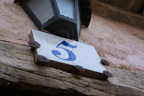 Square white ceramic brick on old wall with the number five painted in blue.. Stock Photos