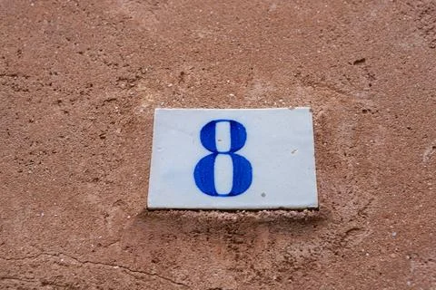 Square white ceramic brick on old wall with the number eight painted in blu.. Foto stock